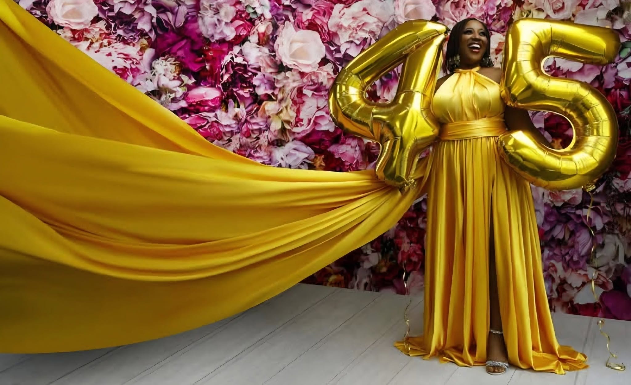 Flying dress — gold gown, floral backdrop, 45 balloons
