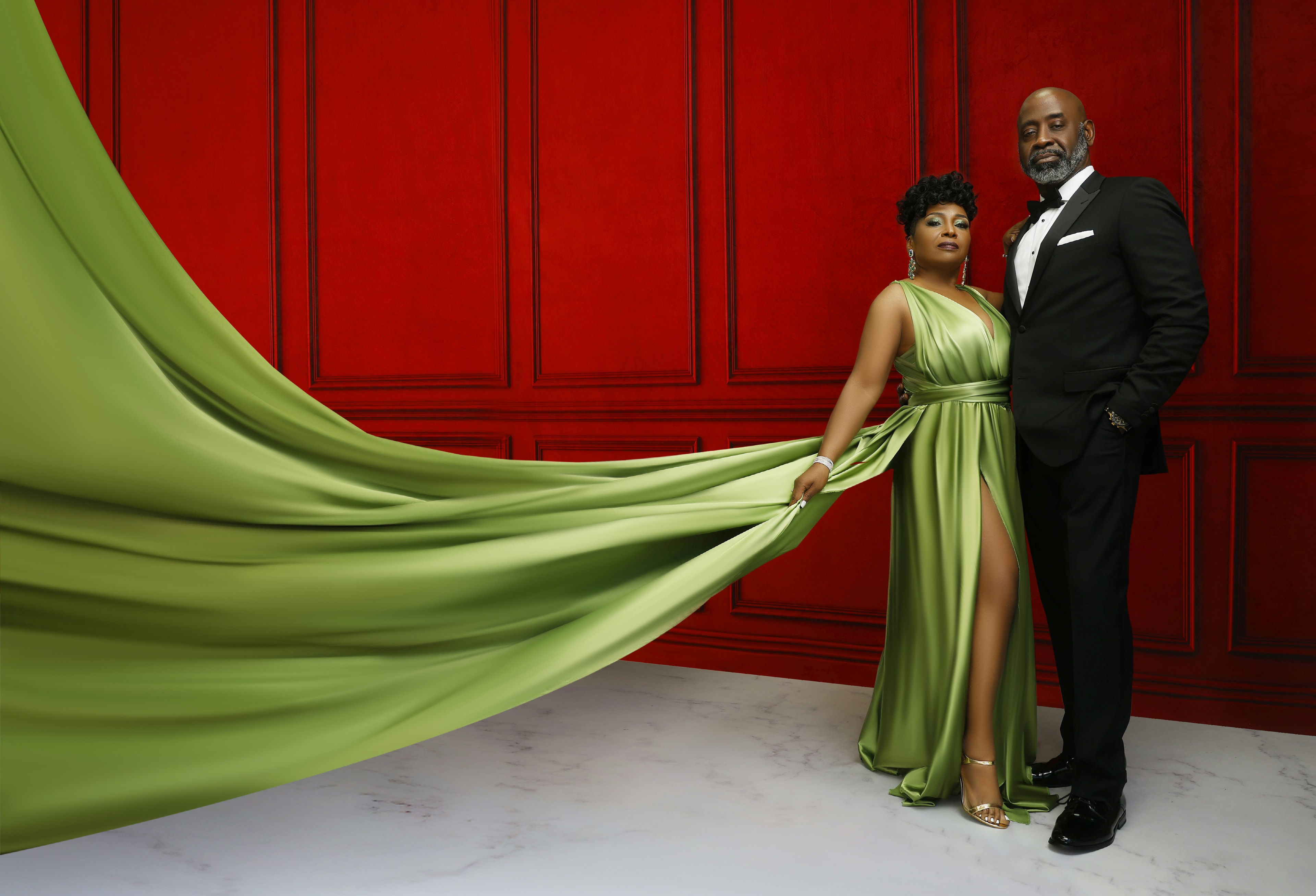 Nannette Ray — green gown with flowing fabric, red wall backdrop, couple portrait