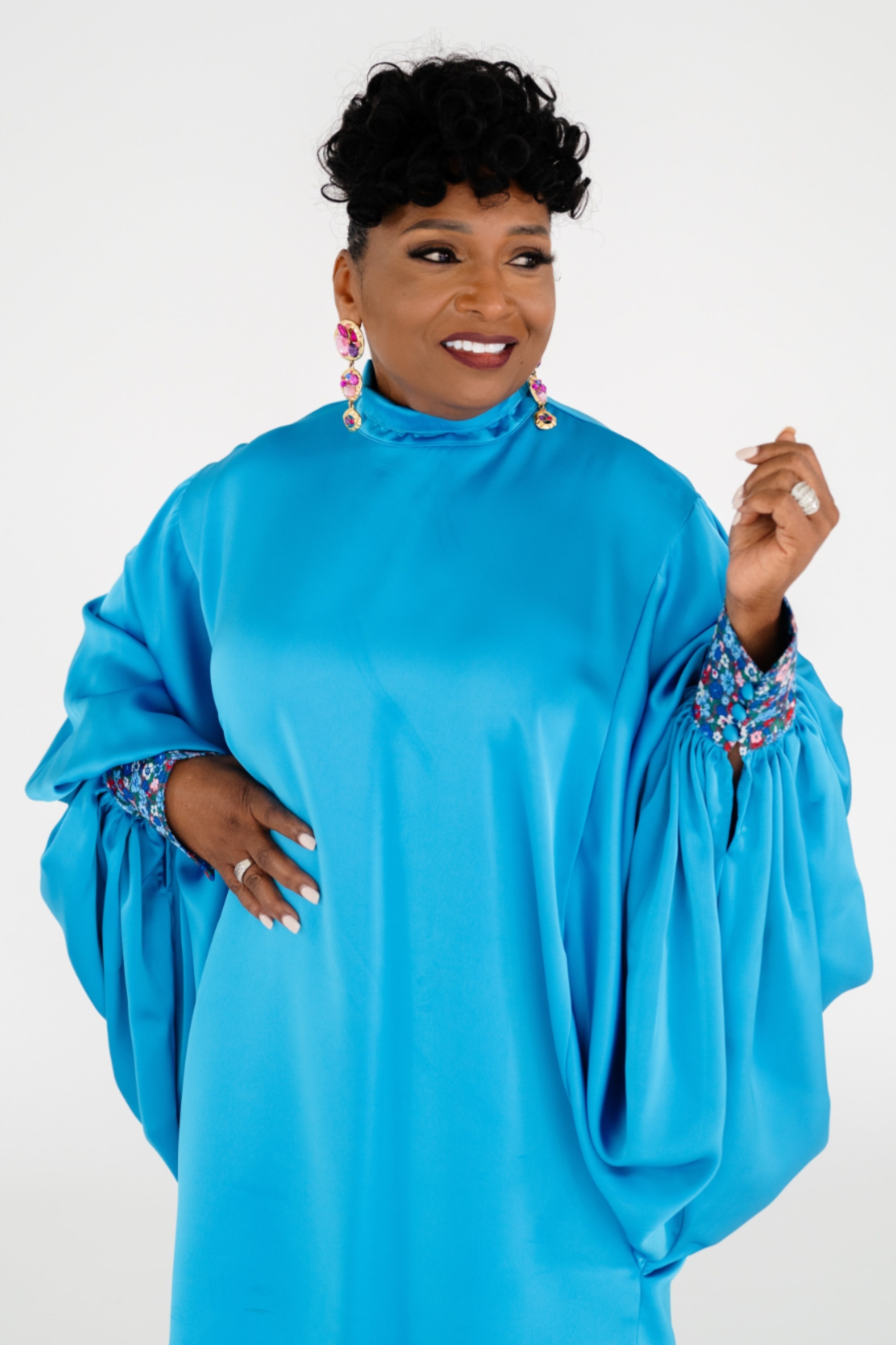 Nannette Ray — blue satin cape dress, standing, joyful expression, solo portrait